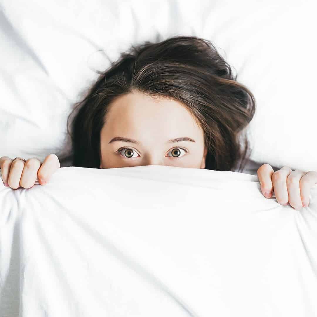 yatakta yeni uyanmış siyah saçlı saklanan bir kadın